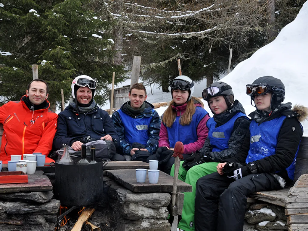 Gruppe sitzt mit Bechern an einem Tisch vor der Hütte.